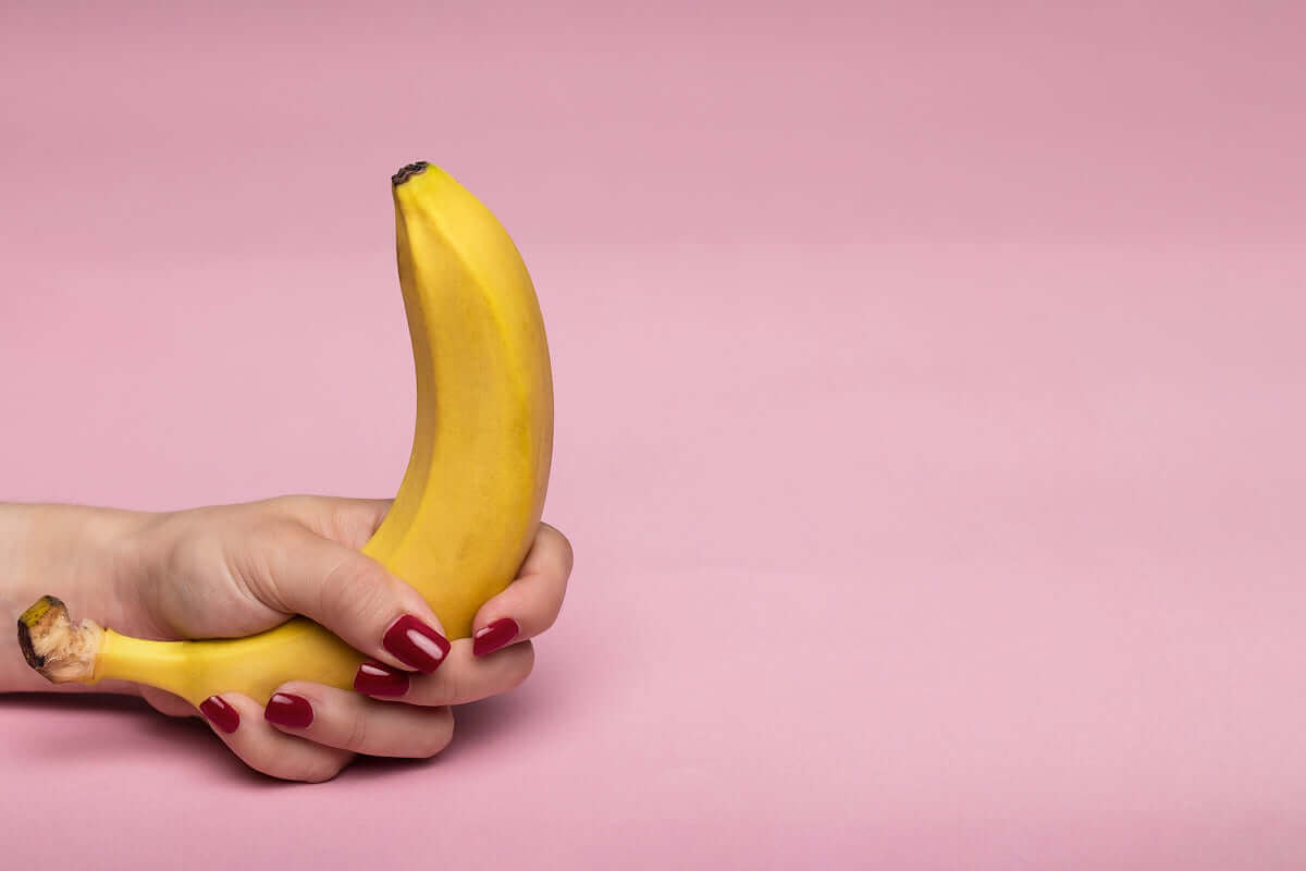 Hand holding a banana against pink background, playful metaphor for Sweety G-Spot vibe pleasure guide