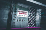Πινακίδα σε δρόμο με μήνυμα “NO SEXUAL SERVICES” μπροστά σε μεταλλικό τοίχο, άρθρο Natura menstrual panty super βιώσιμη περίοδος