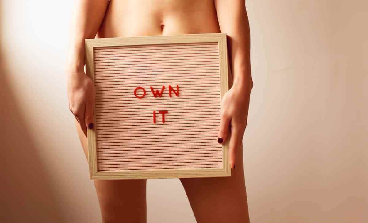 Own It framed sign held by a person, featuring red letters on a striped background.
