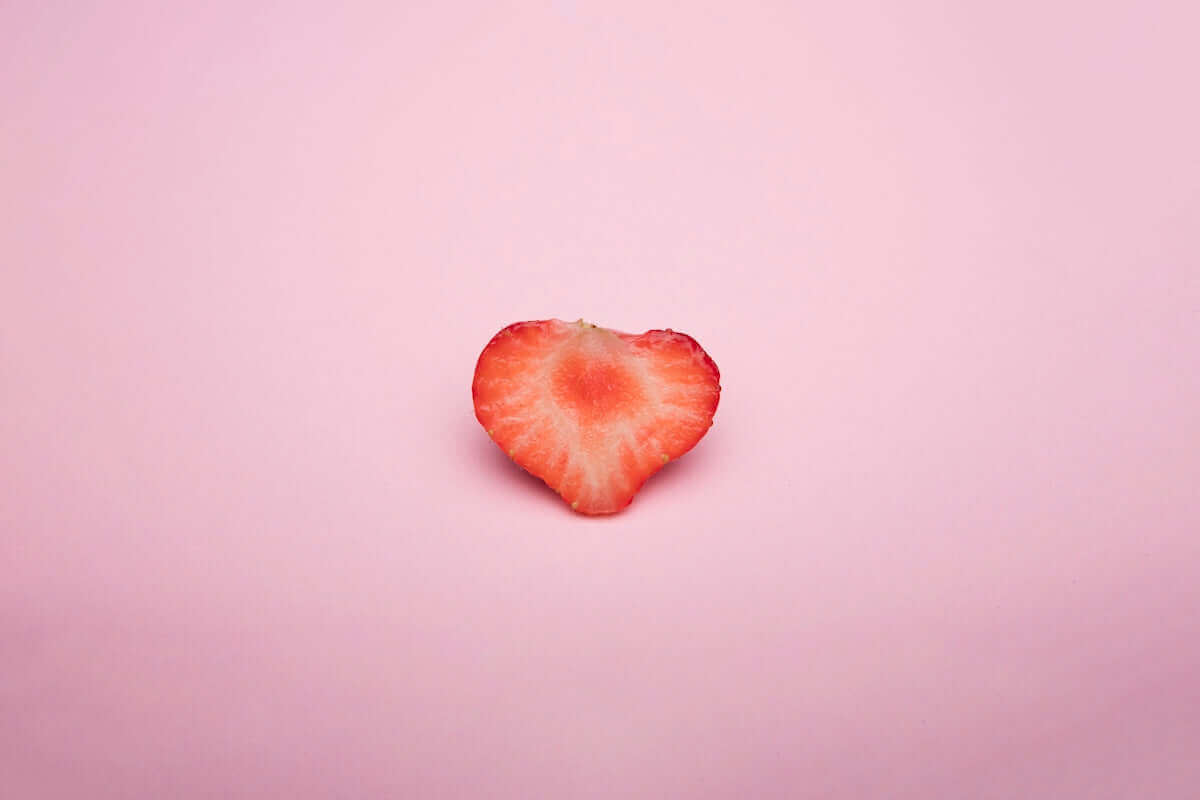 Alt Tag: Heart-shaped strawberry slice on pastel pink background illustrating sweetness in a vintage wind up dolls themed article cover