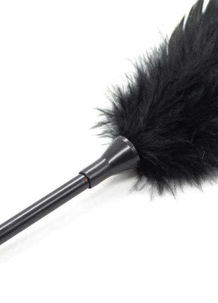 Feather Tickler and Paddle with a slim black handle and a large, fluffy black feather head