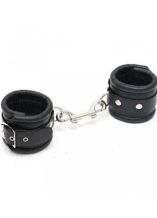 Feet Cuffs LUX 7 CM featuring two black padded cuffs with adjustable buckled straps and a connecting metal chain.
