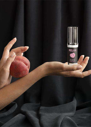 Relax! Anal Gel in a slim black bottle with a silver cap and pink label, displayed beside a peach-shaped object
