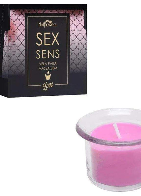 Scented Massage Candle Love in a clear glass holder, with vivid pink wax and a single white wick, beside patterned black packaging