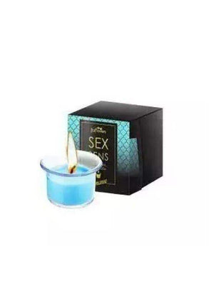 Scented Massage Candle Romance in a clear glass cup with bright blue wax and a lit wick beside a black patterned box